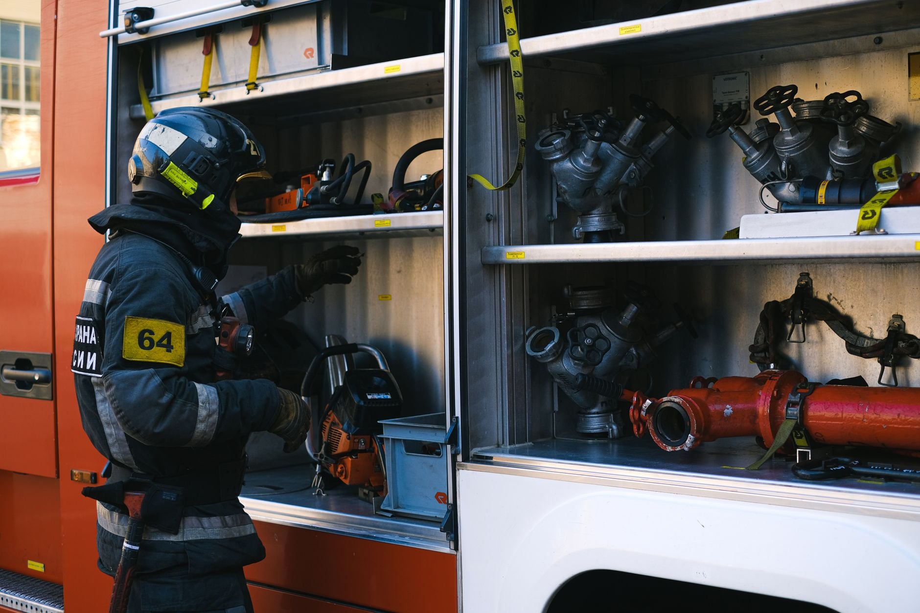 Firefighter arranging equipment and tools in a fire engine's compartment.