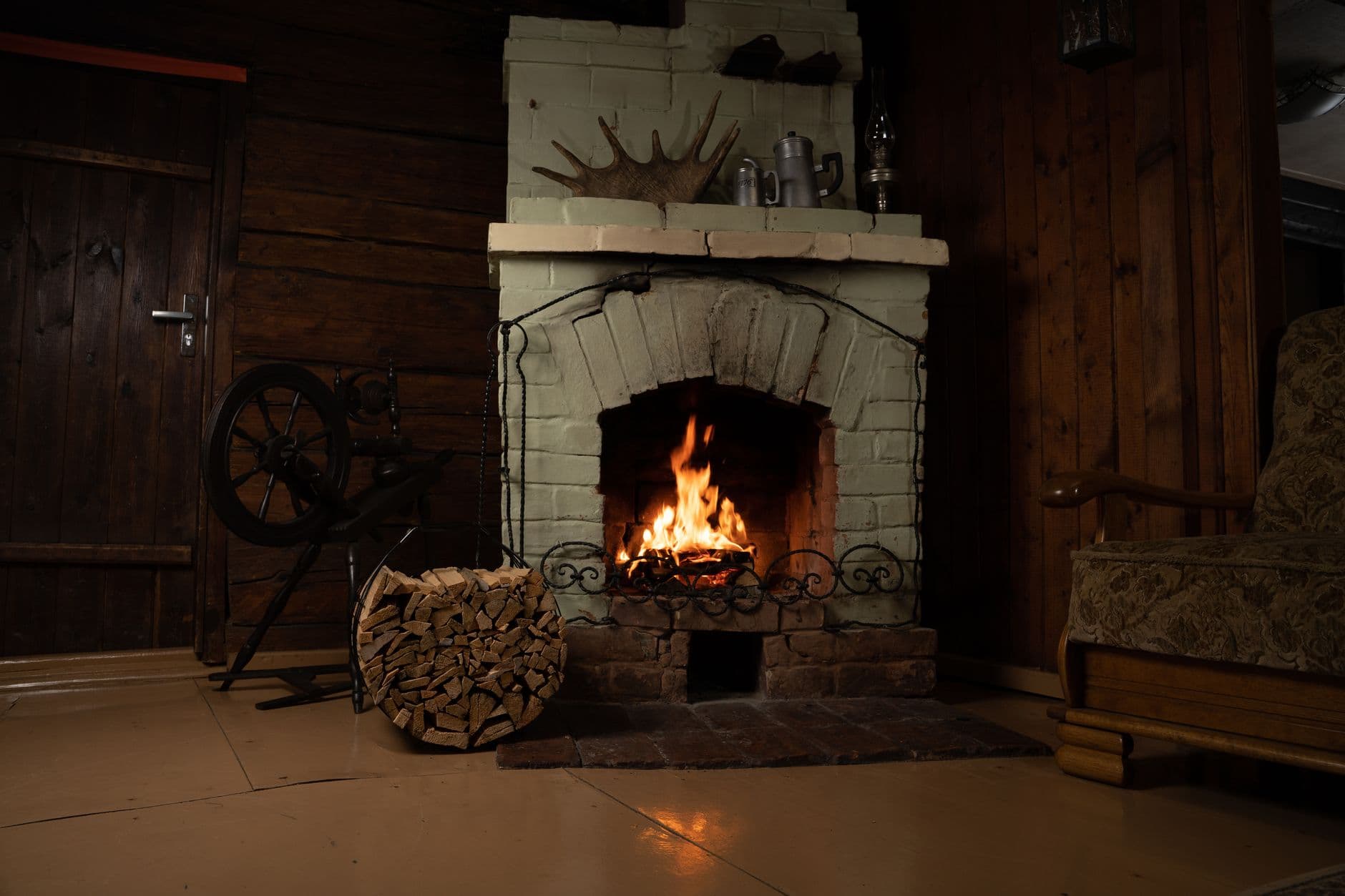 Warm rustic room featuring a brick fireplace with roaring fire, logs, and vintage decor.